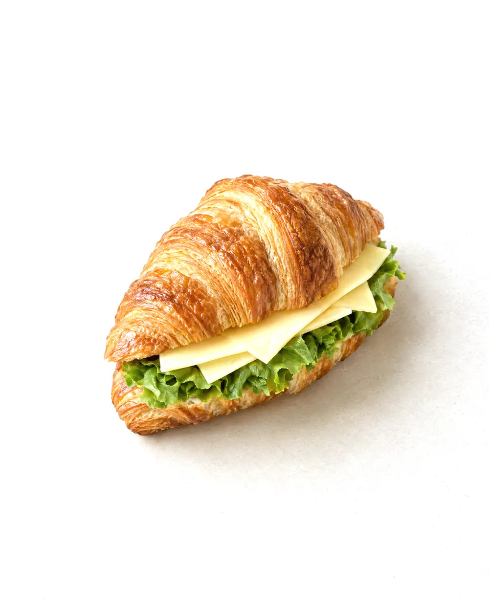 Concept image of a croissant sandwich: a sliced croissant with a layer of green lettuce and sliced cheese.