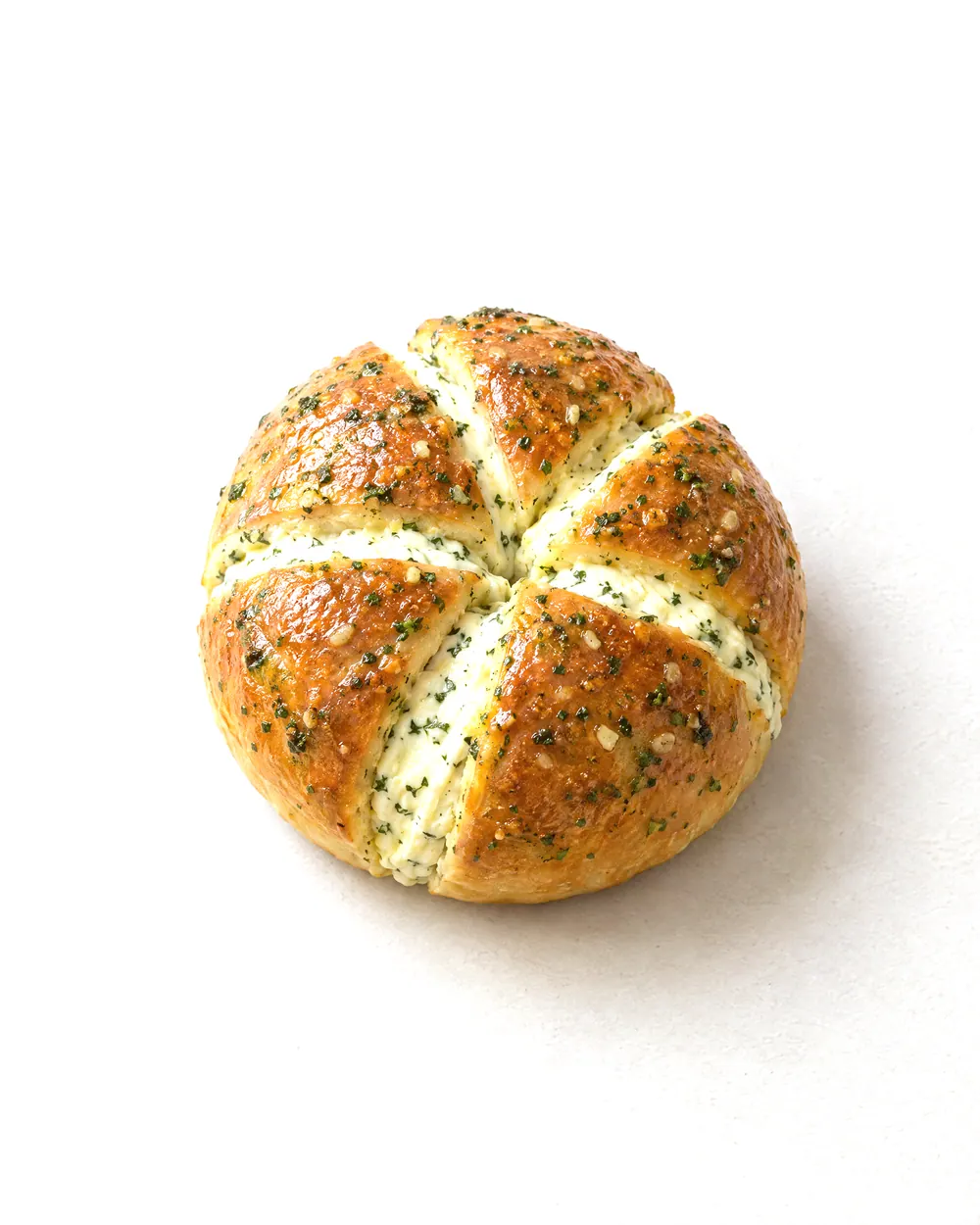 Concept image of garlic cream cheese bread: a round bun cut into six wedges with cream cheese between them, flecked with green herbs.