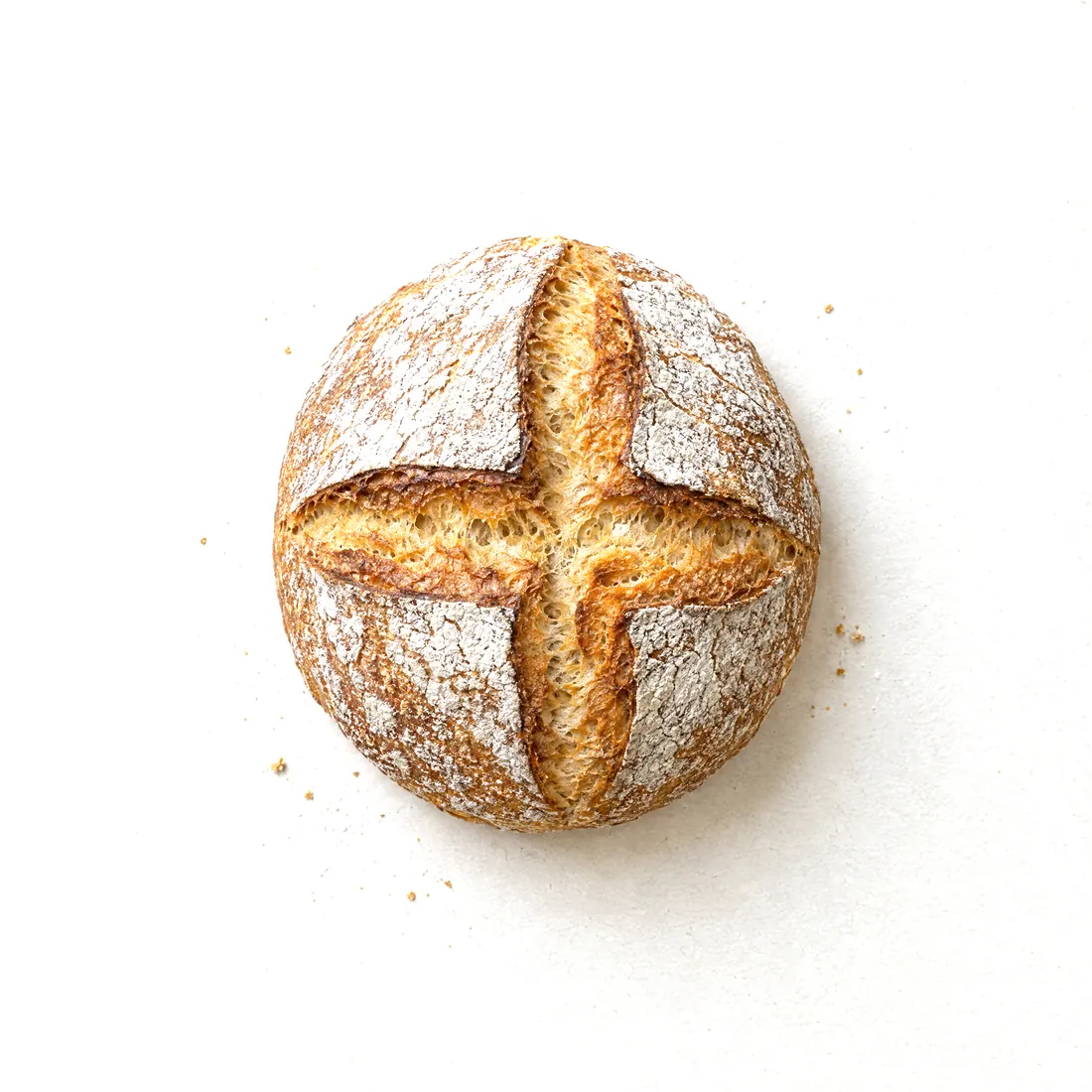 Concept image: a round country loaf with a floured, cross-scored crust, seen from above on paper.