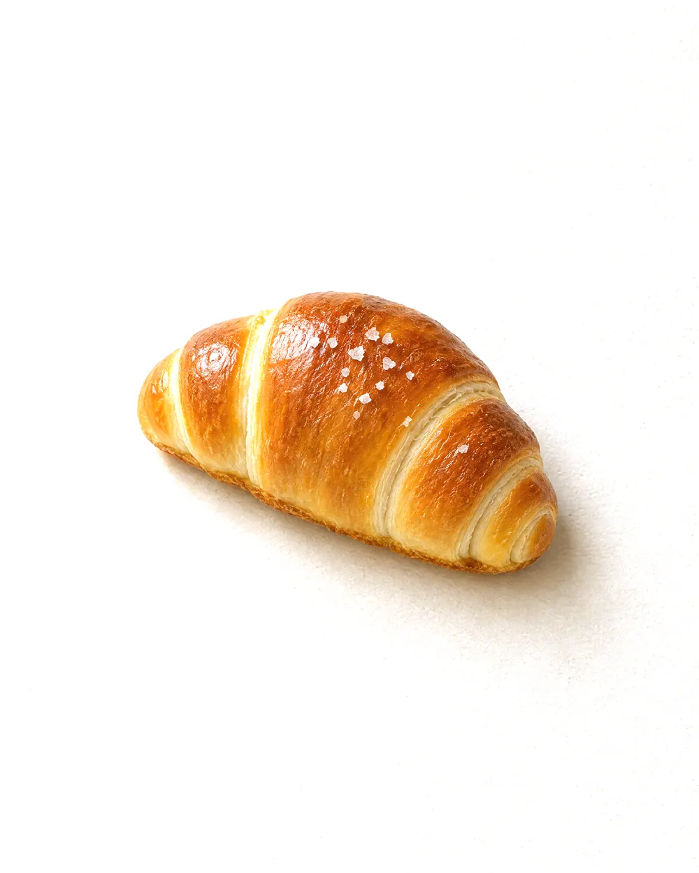 Concept image of salt bread: a glossy golden rolled bun with a few flakes of coarse salt, on plain paper.