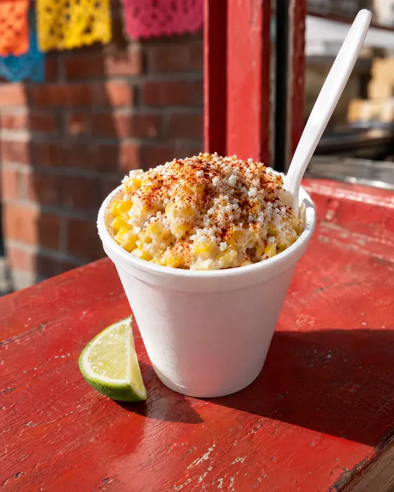 A cup of esquite with cotija, chili powder and a lime wedge.