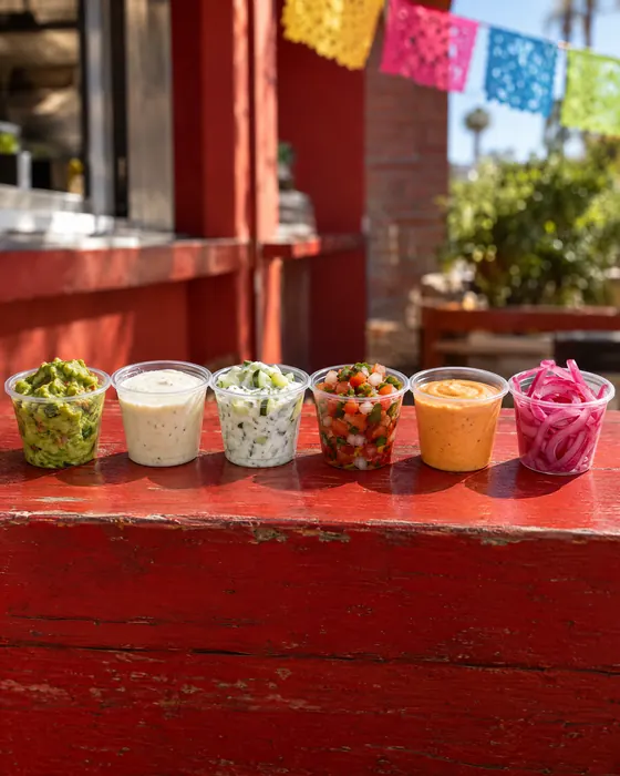 Six small cups of sauces and toppings in a row.