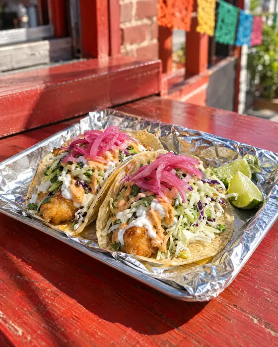 Two fish tacos with cabbage, sauces and pickled onions.