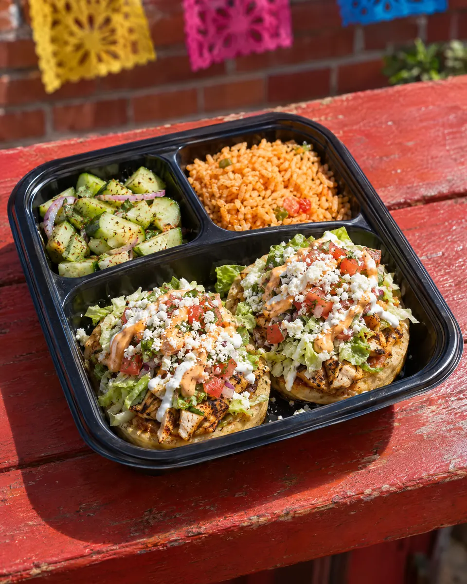 Sopes Plate: two sopes topped with chicken, lettuce, pico de gallo, sour cream and cotija, with cucumber salad and rice.