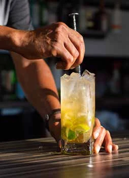 Hands stirring a tall cocktail over ice at the bar