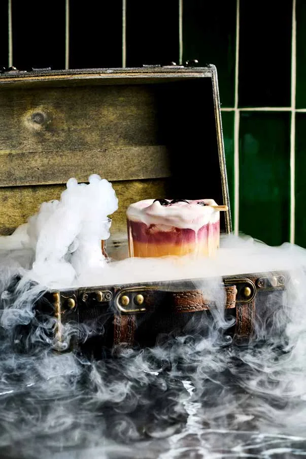 La Manzana Whiskey Sour in an open treasure chest spilling dry-ice smoke, against green tile