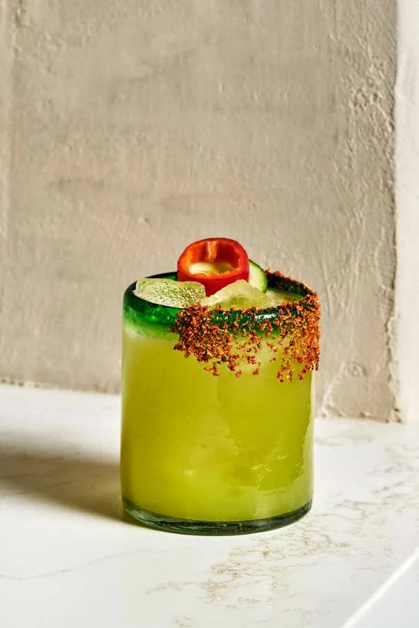 Spicy Margarita Balagán in a green-rimmed glass with a Tajín rim, a red Fresno chile and cucumber