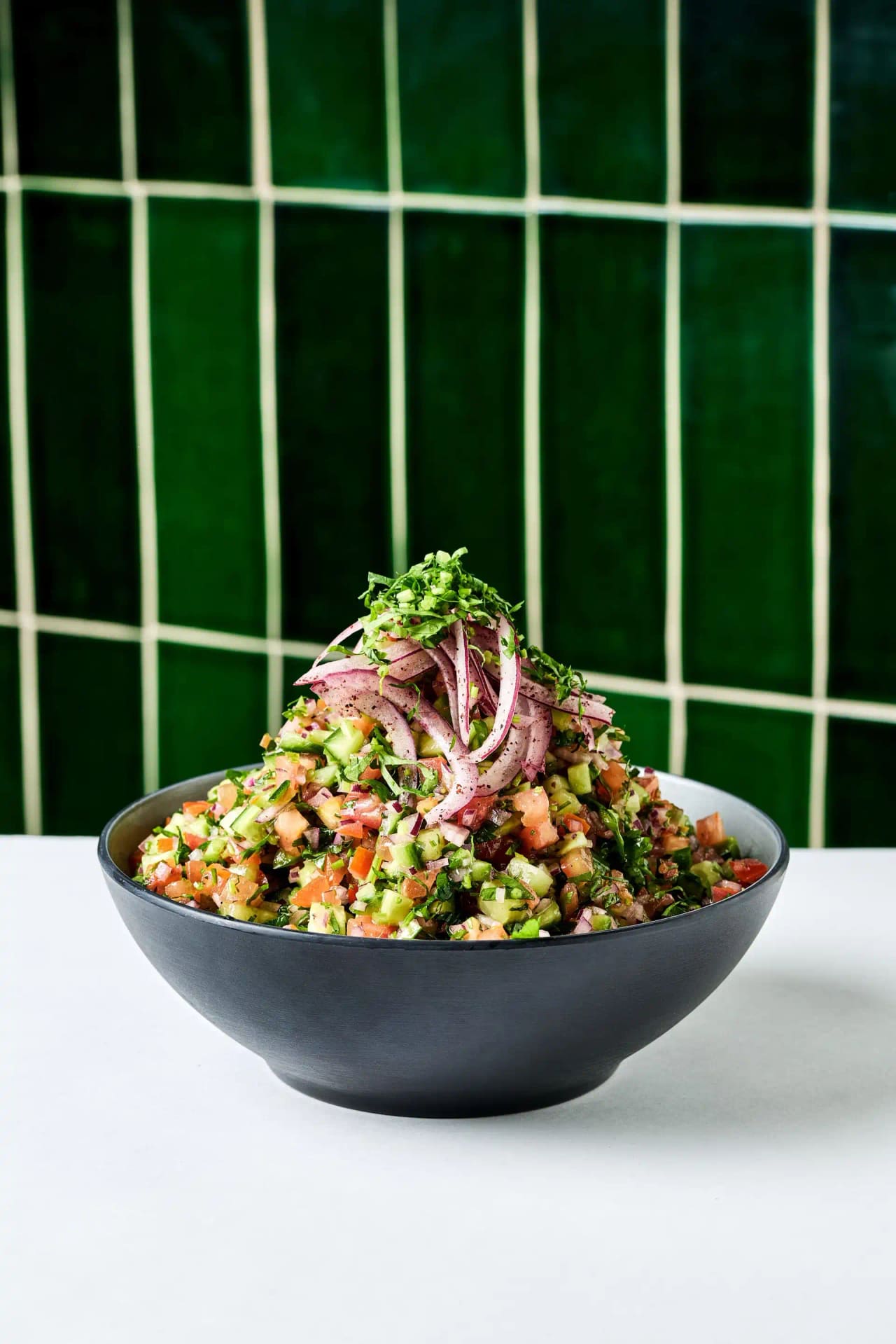 Dark bowl of chopped tomato and cucumber salad topped with red onion