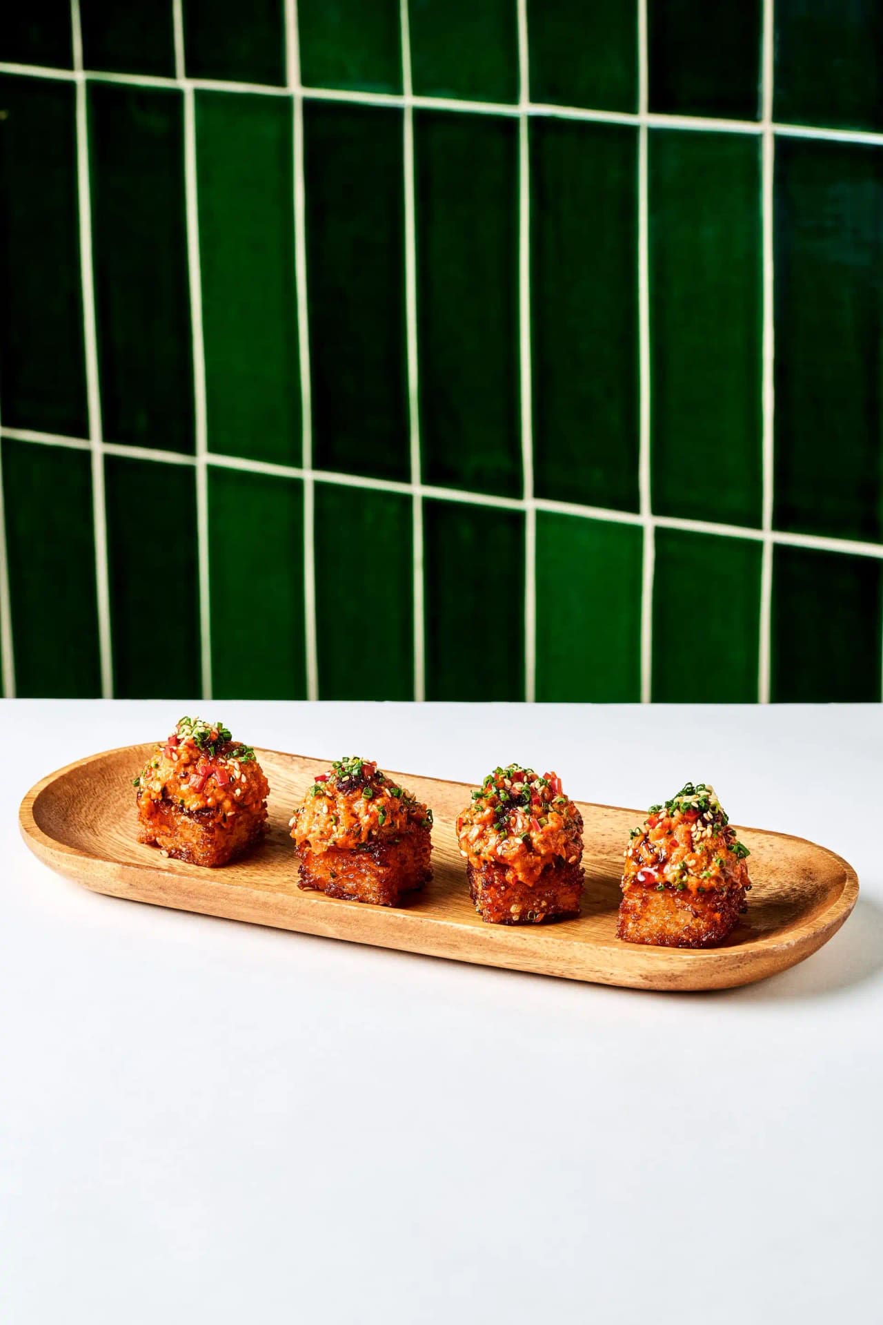 Four crispy bites topped with salsa on a long wooden tray