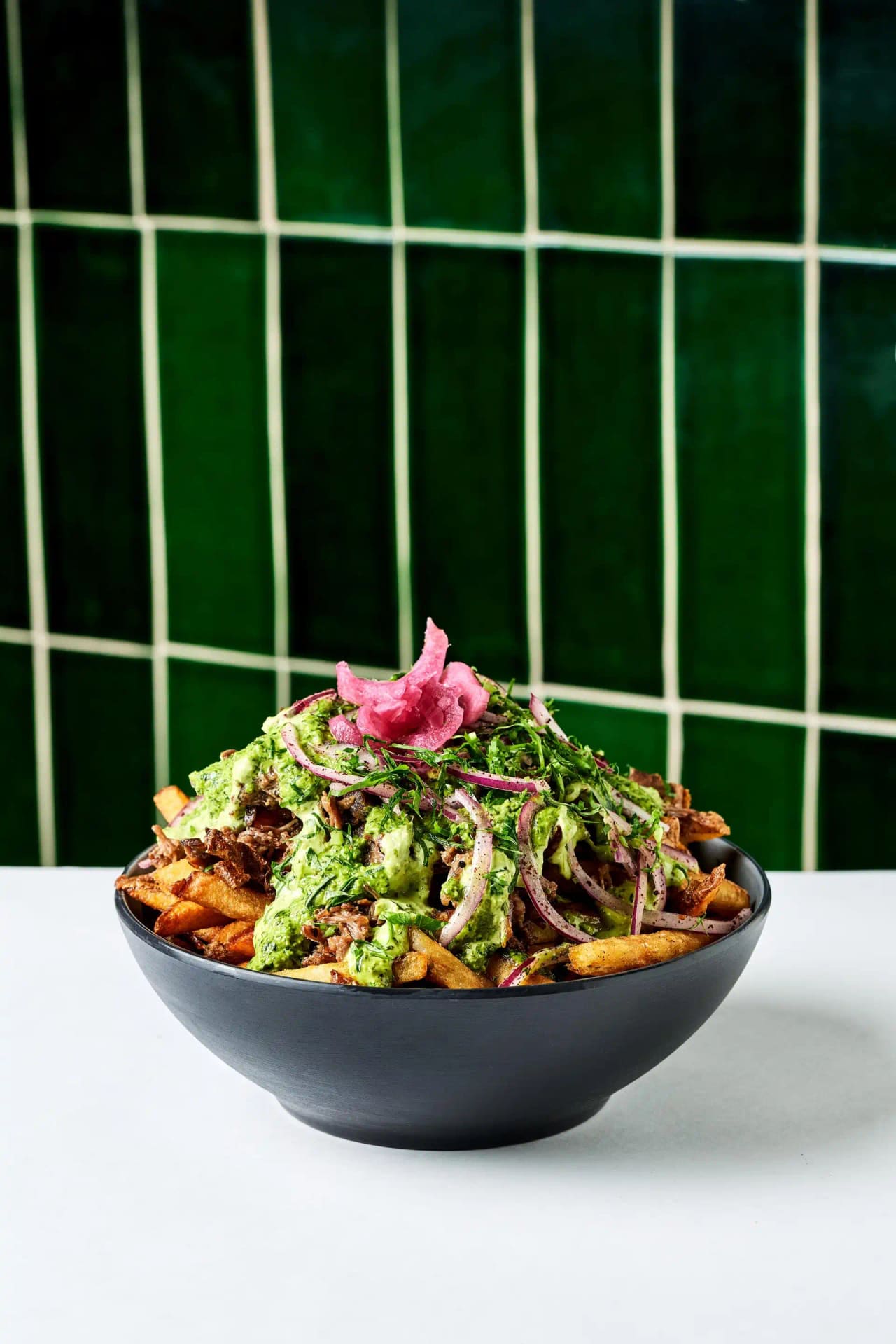 Bowl of fries covered in pulled brisket, chimichurri and pickled onion