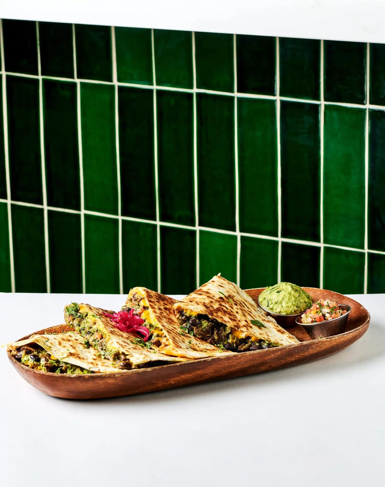 Sliced quesadilla on a wooden board with guacamole and pico de gallo
