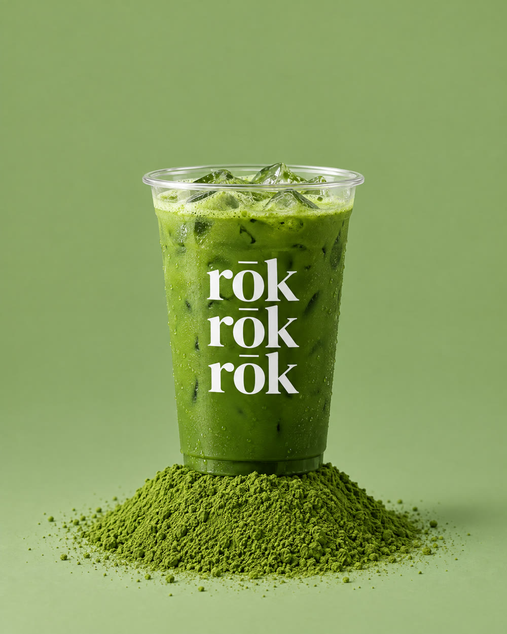 A rōk cup of iced matcha standing on a mound of matcha powder