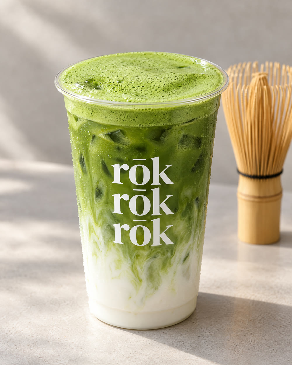 Iced matcha latte in a rōk cup with a bamboo whisk behind it