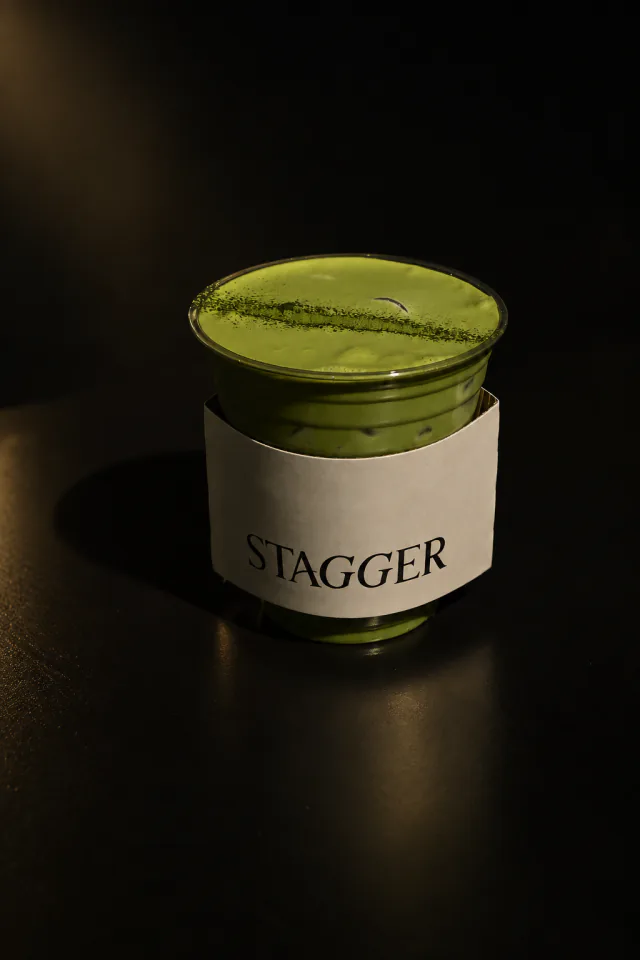 An iced Stagger matcha latte in a cream Stagger sleeve, lit against a dark surface