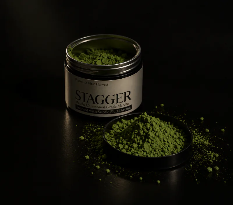 An open Stagger matcha tin beside its lid, piled with bright green matcha powder
